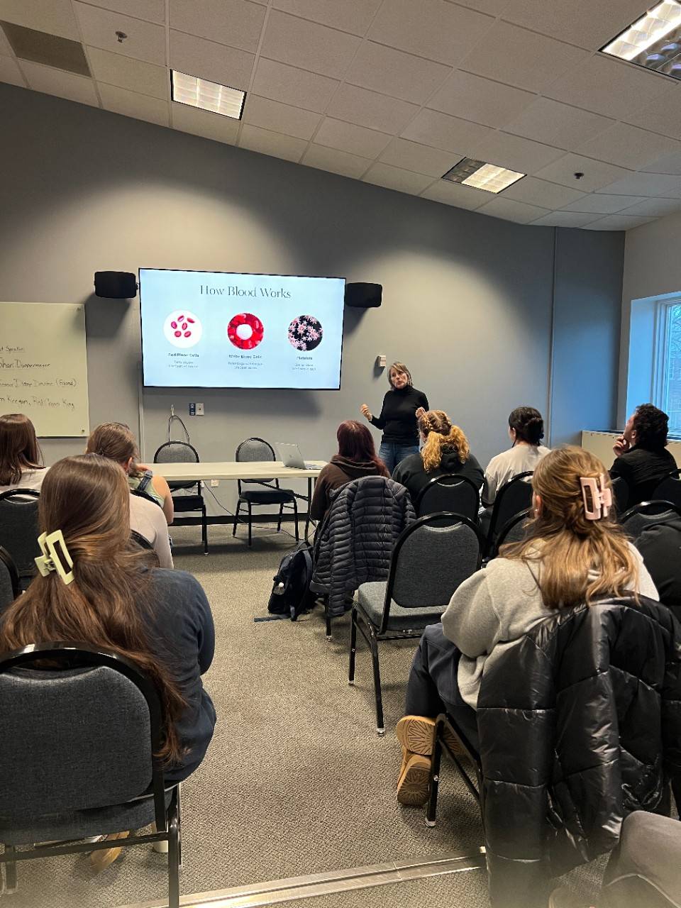 Woman presents presentation about blood donation to a room of people