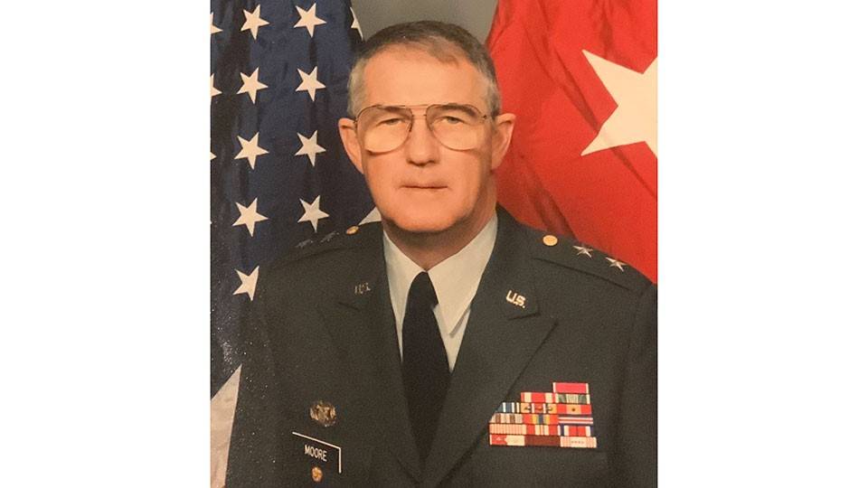 Buddy Moore in military uniform stands proudly beside an American flag.