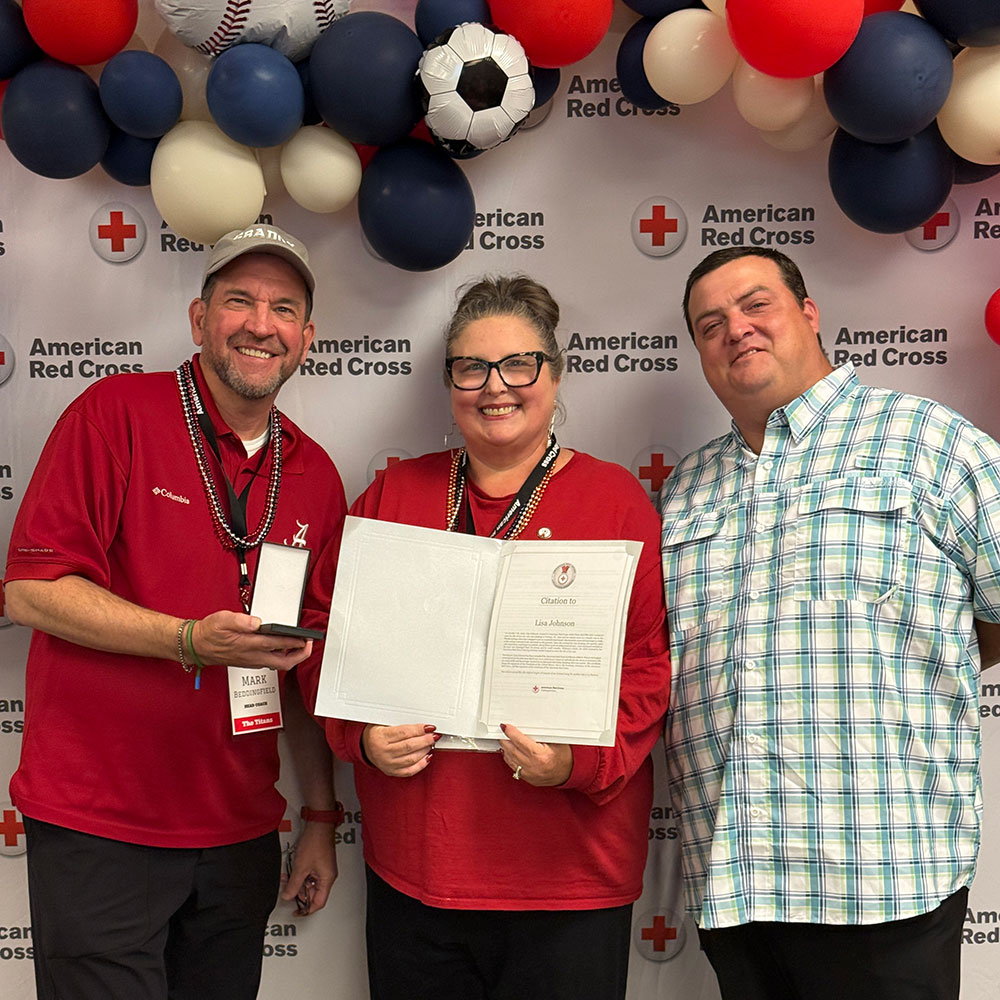 Lisa Johnson holding a Red Cross award, with her husband and a Red Cross staff member standing next to her.