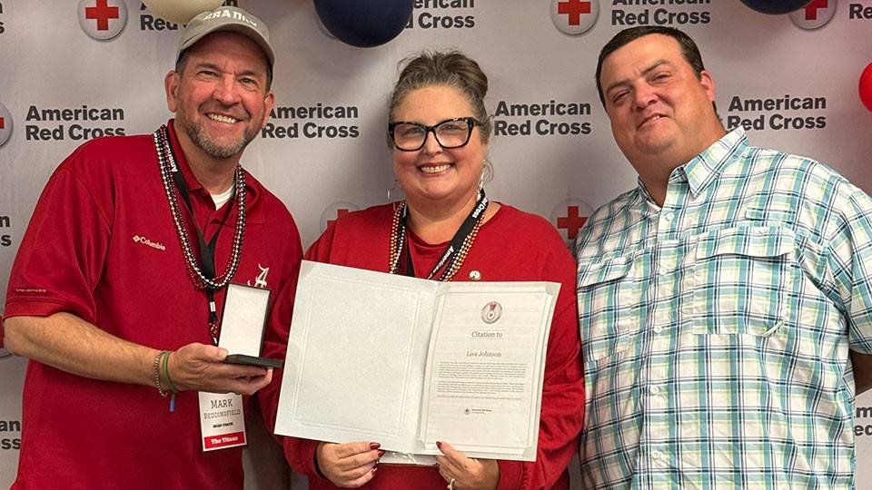 Lisa Johnson holding a Red Cross award, with her husband and a Red Cross staff member standing next to her.