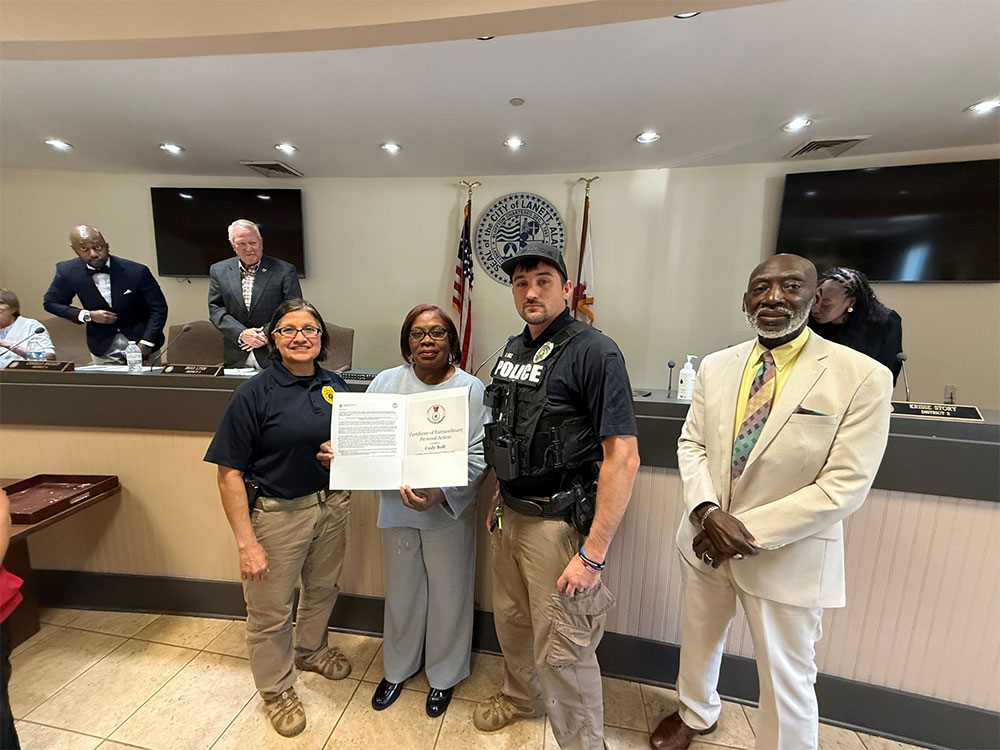 Officer Cody Bolt holding the American Red Cross Certificate of Extraordinary Personal Action with other officers and staff in the room.