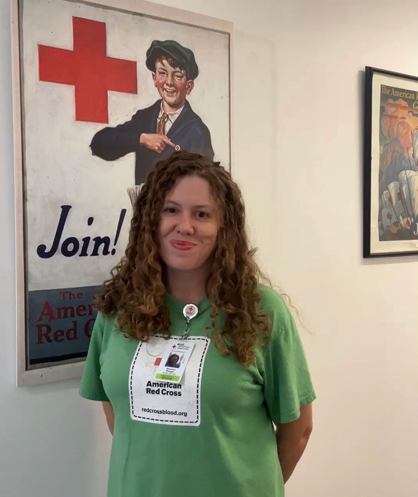 Shannon Pinega smiling while standing next to a Red Cross promotional poster on a wall.
