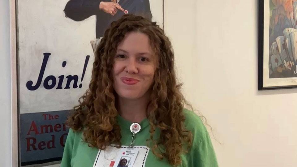 Shannon Pinega smiling while standing next to a Red Cross promotional poster on a wall.