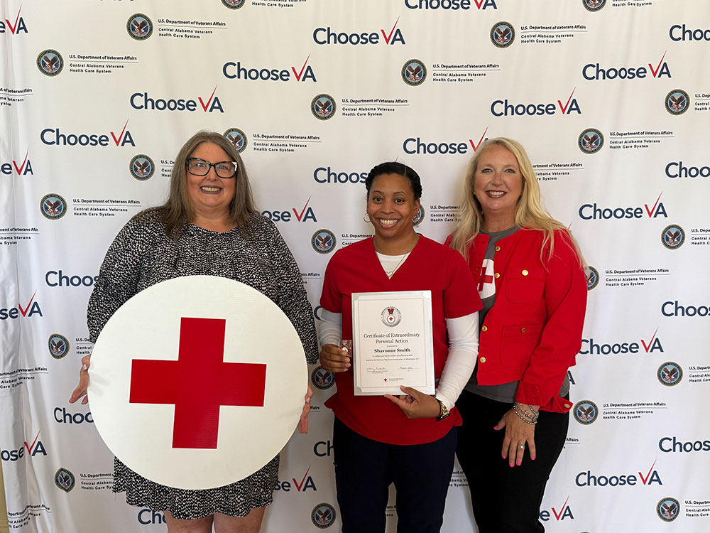 Shavonne Smith, standing next to two women, holding the Red Cross certificate of extraordinary personal action.