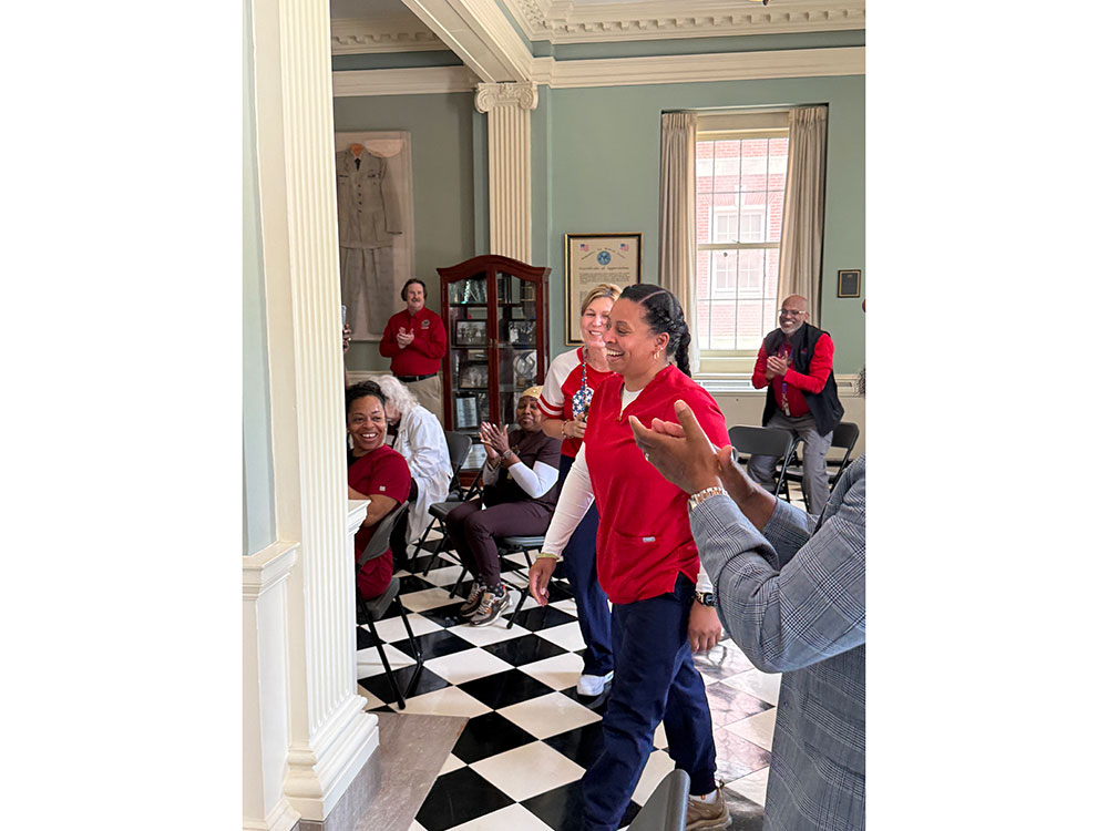 People in red cross shirts applaud Shavonne Smith as she walks through a room.
