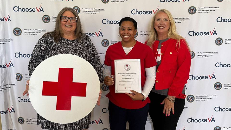Shavonne Smith, standing next to two women, holding the Red Cross certificate of extraordinary personal action.