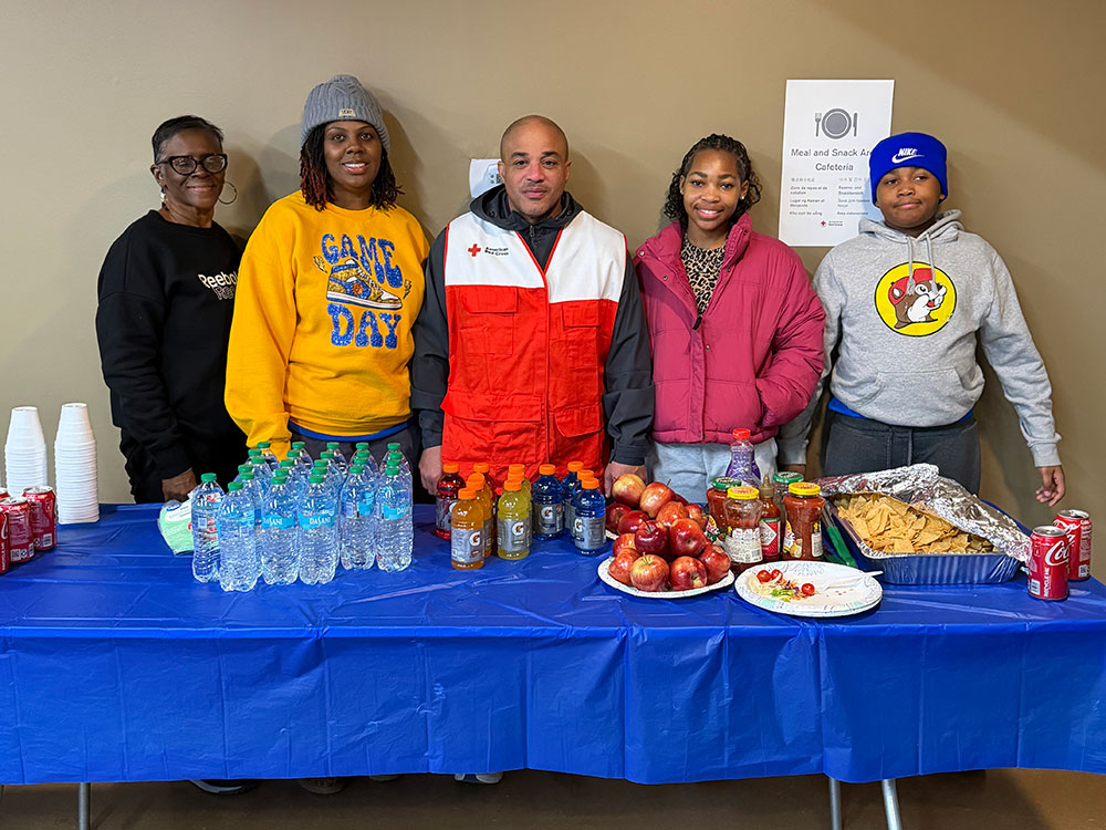 Group of Red Cross volunteers standing behind a table with water and food.