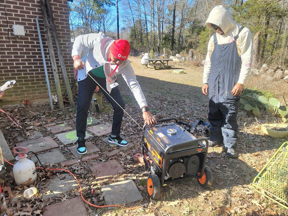 Two Red Cross volunteers starting up a generator in someone's yard.