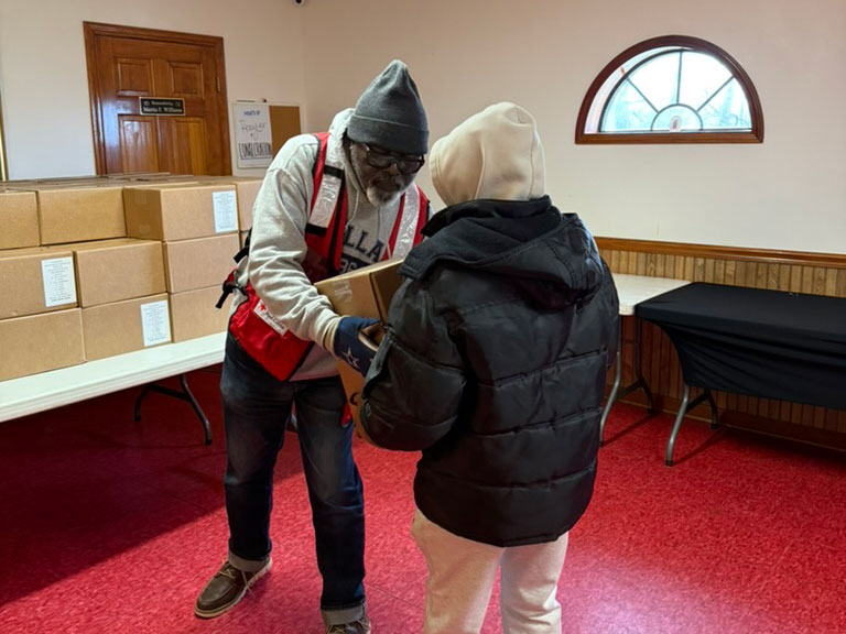 Red Cross volunteer handing a box to another person.