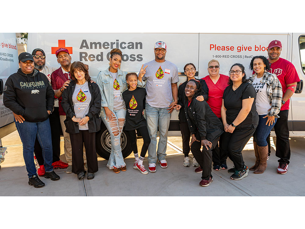 Dr. Aja Murphy, her daughter, and a diverse group of smiling people stands in front of an American Red Cross blood donation van.