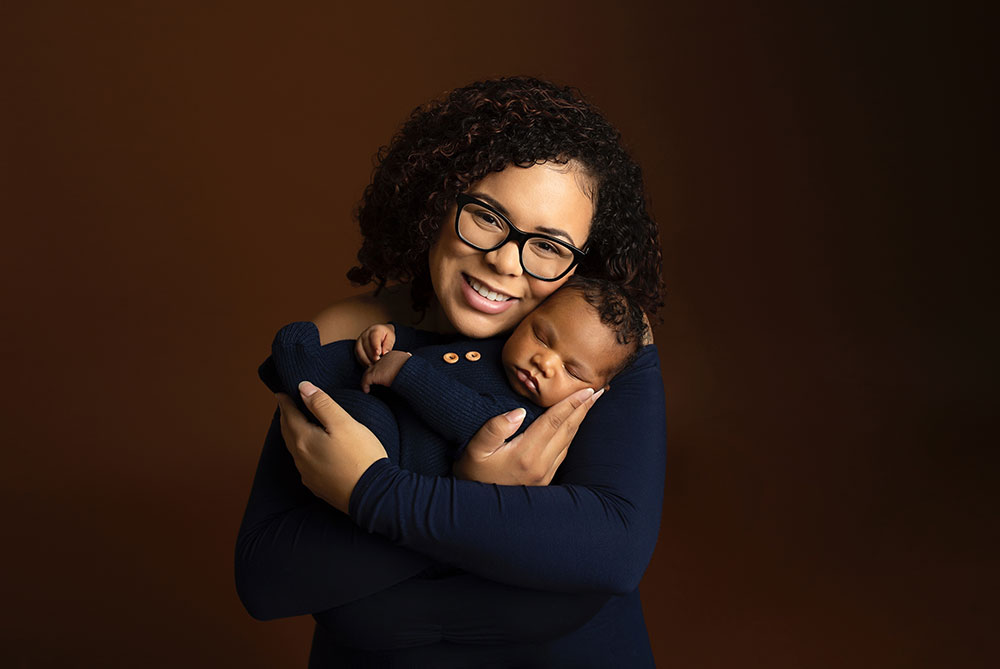 Angelena Fly holding her sleeping baby and smiling.