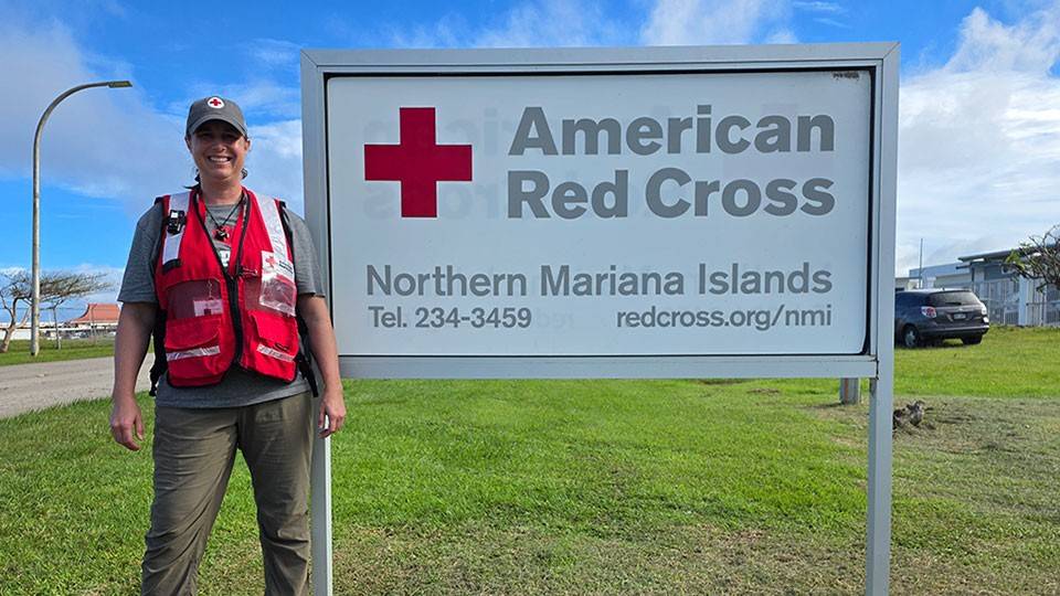 Red Cross volunteer Caroline Scudder standing in front of a an American Red Cross Northern Mariana Islands sign on the grass.