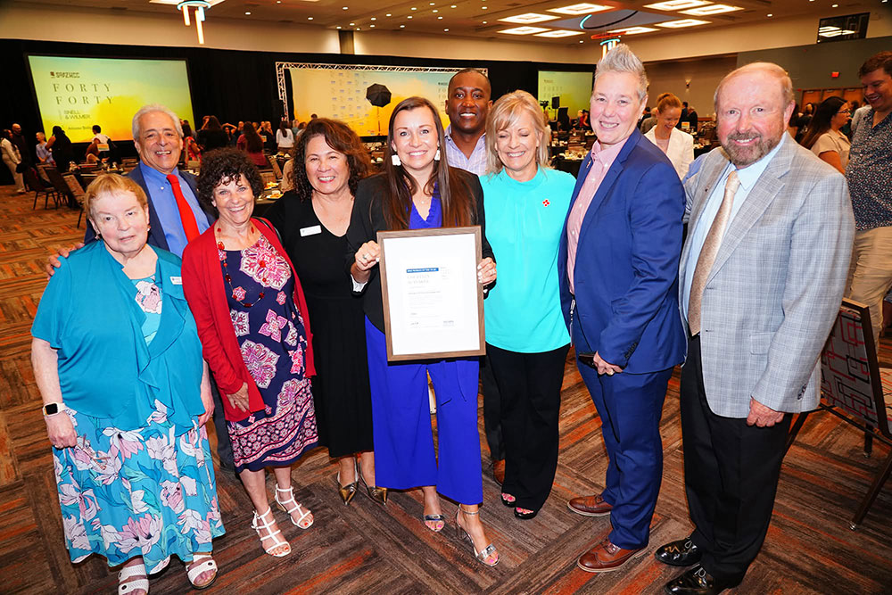 Courtney Slanaker holding award while surrounded by eight red cross staff members at an event.