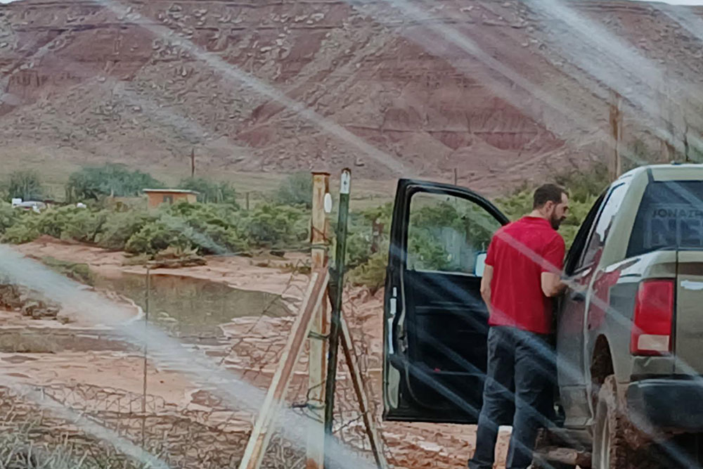 a man standing next to a truck with flood waters in a muddy area in front of him.