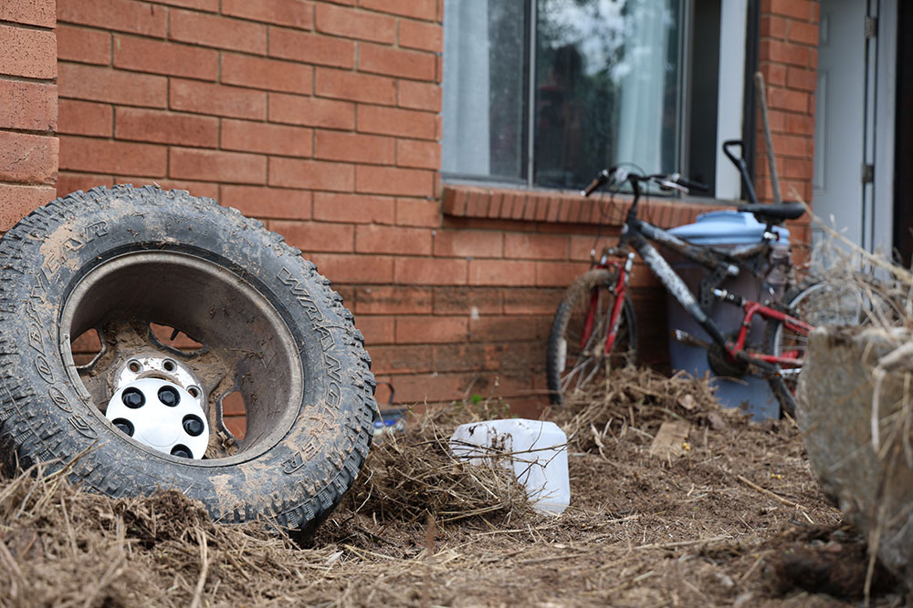 a spare tire, bike, trash can and debris next to a brick house.