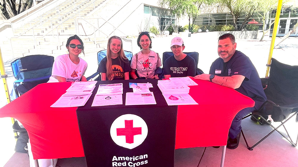 a group of red cross volunteers sitting at a table outside with red cross pamphlets laid out on the table.