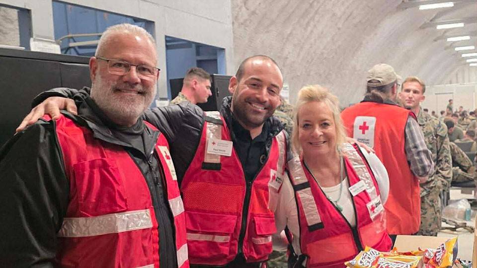 Tami and Paul Smith and Paul Smith Jr., wearing red cross volunteer safety vests, take a group photo while next to boxes with chips.