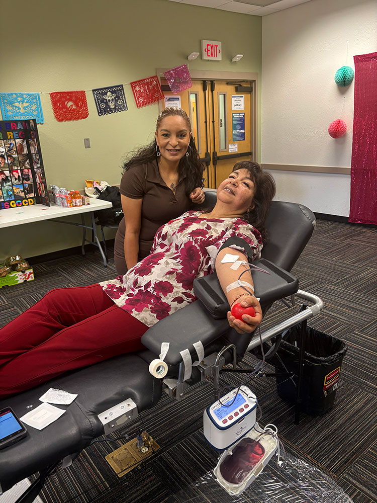 Reina Nunez standing next to a person who is in a chair donating blood.