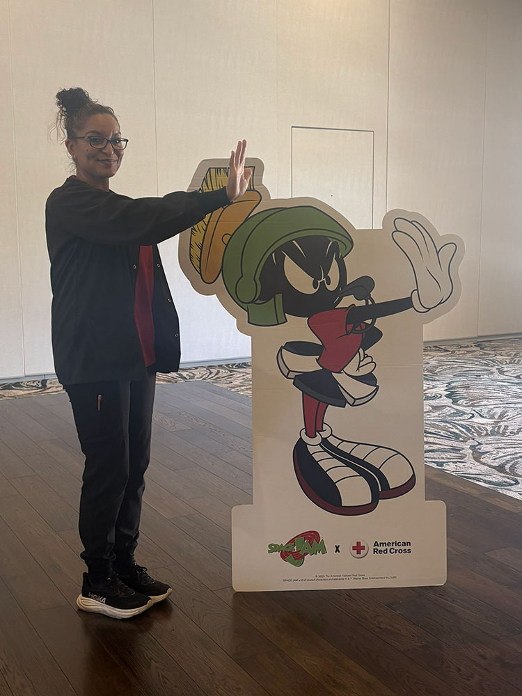 Reina Nunez holding her arm out while standing next to a cardboard cutout of the Looney Tunes character Marvin the Martian.