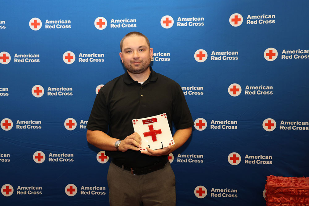 Red Cross volunteer Scott Saltzer holding a Red Cross award at a Red Cross event.