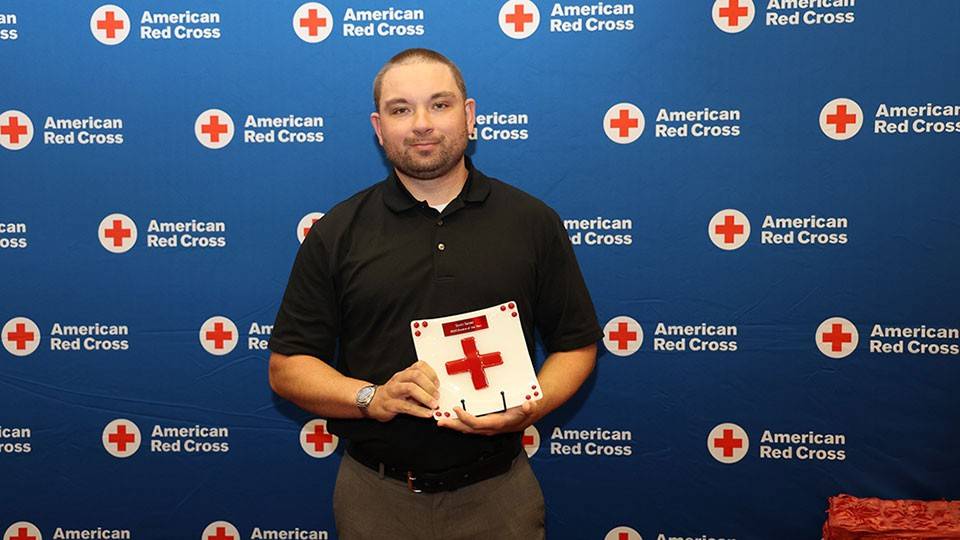 Red Cross volunteer Scott Saltzer holding a Red Cross award at a Red Cross event.