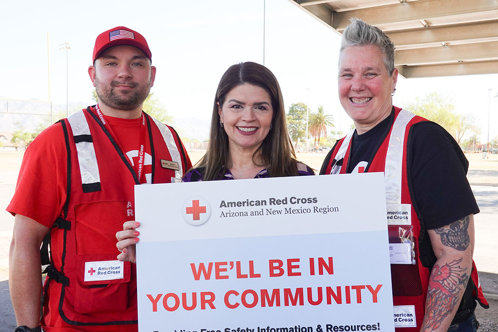 Scott Salzer and two other people holding a red cross sign that says, "We'll be in your community".