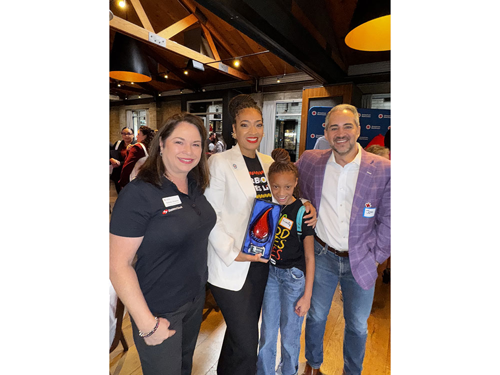Dr. Aja Murphy, her daughter, and two other people stand together smiling in a warmly lit room. Dr. Aja Murphy holds an award.