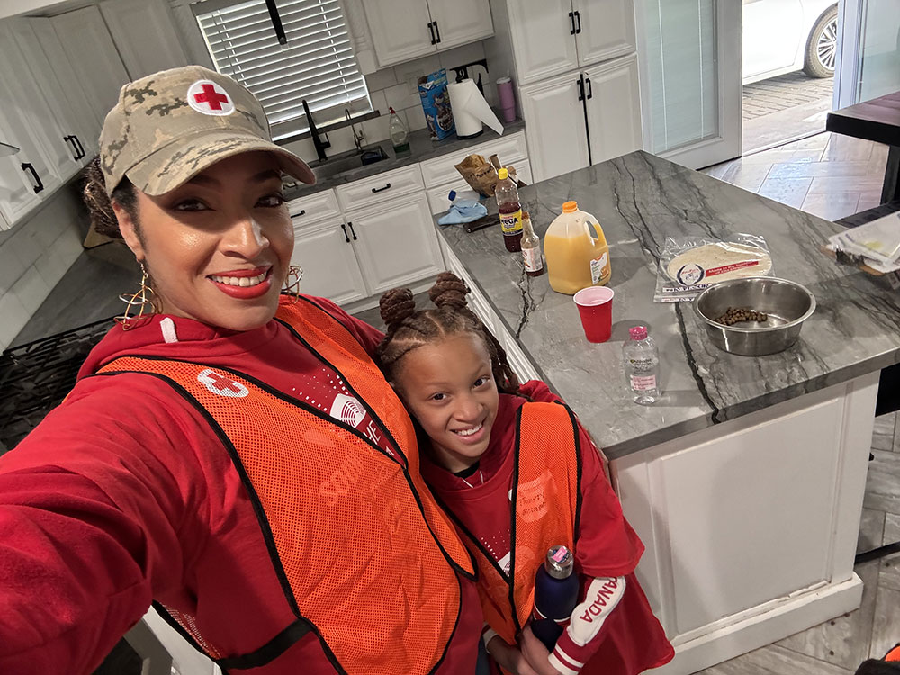 Smiling Dr. Aja Murphy and her daughter in orange safety vests stand in a kitchen. Countertop with food items and drinks.