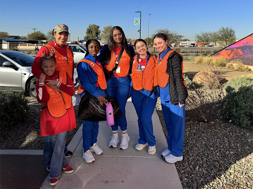 Dr. Aja Murphy, her daughter, and four volunteers stand outdoors, smiling. They wear blue uniforms and orange safety vests.