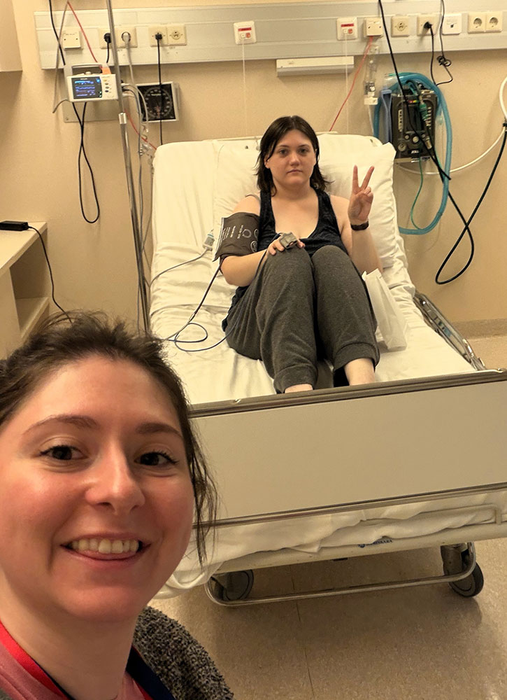 Ama Larson sitting upright in a hospital bed giving the peace sign.
