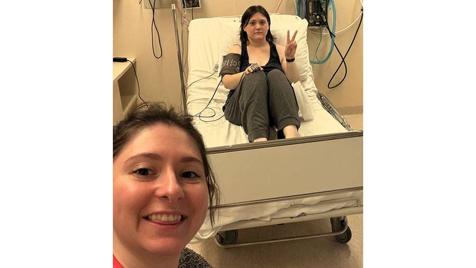 Ama Larson sitting upright in a hospital bed giving the peace sign.