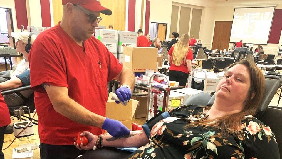 Amber Thomas sitting in a chair about to donate blood at the Red Cross blood drive. A Red Cross nurse is standing next to her.