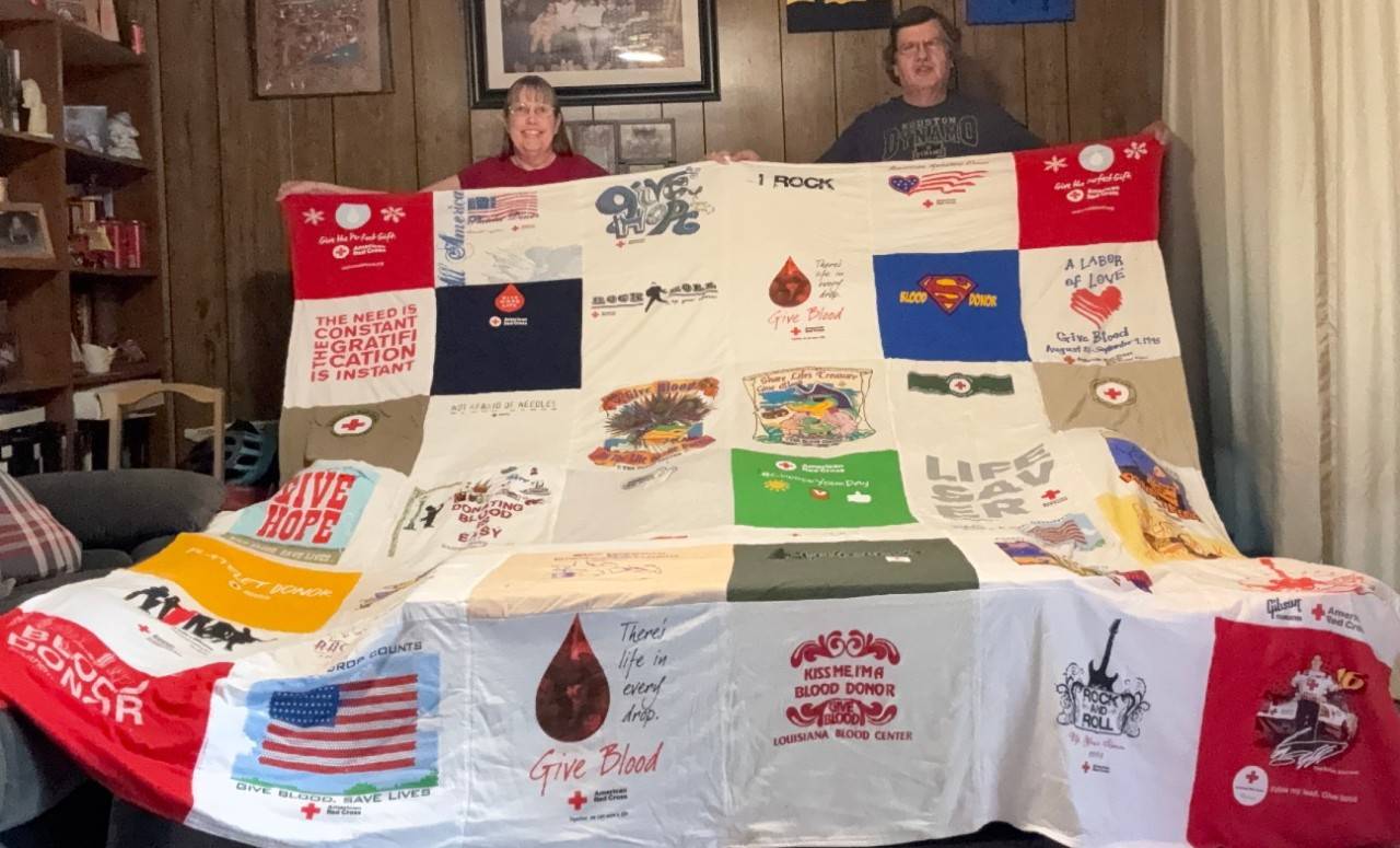 Two Red Cross blodd donors holding up a quilt.