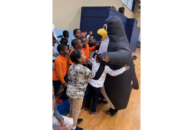 Pedro the penguin mascot hugging school children.