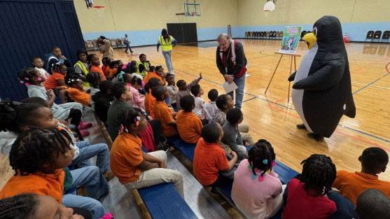 a Red Cross volunteer and Pedro the penguin mascot speak to a room full of school children.