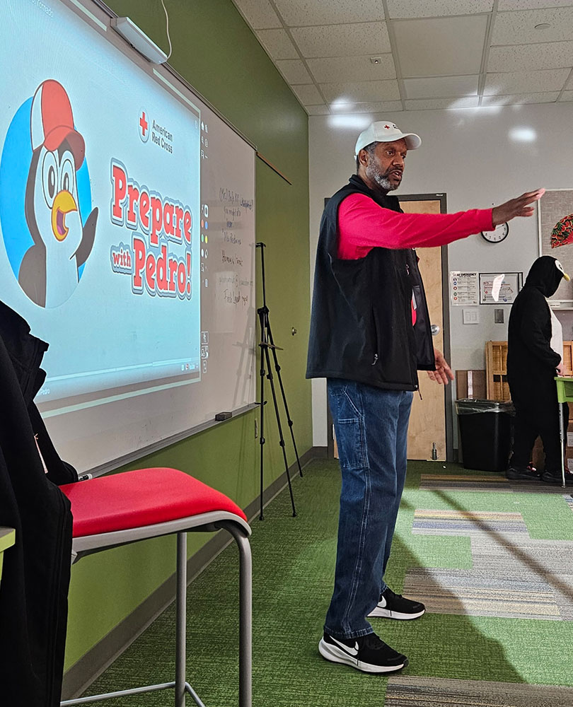 Henry Childress standing at the front of a classroom with prepare with pedro projected on a wall behind him.