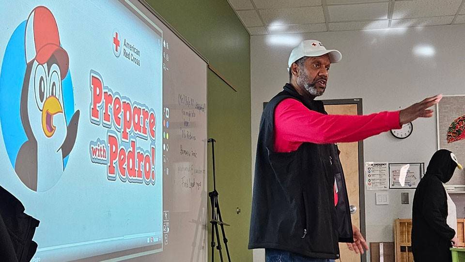 Henry Childress standing at the front of a classroom with prepare with pedro projected on a wall behind him.