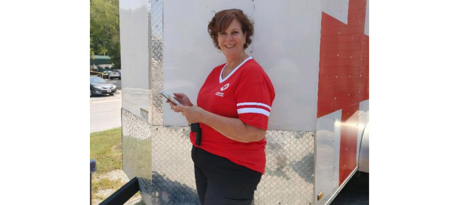 Julie Stolting wearing a Red Cross shirt and standing next to a Red Cross trailer.