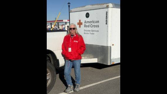 Kim Wilson wearing sunglasses and a Red Cross jacket while standing next to a Red Cross trailer.