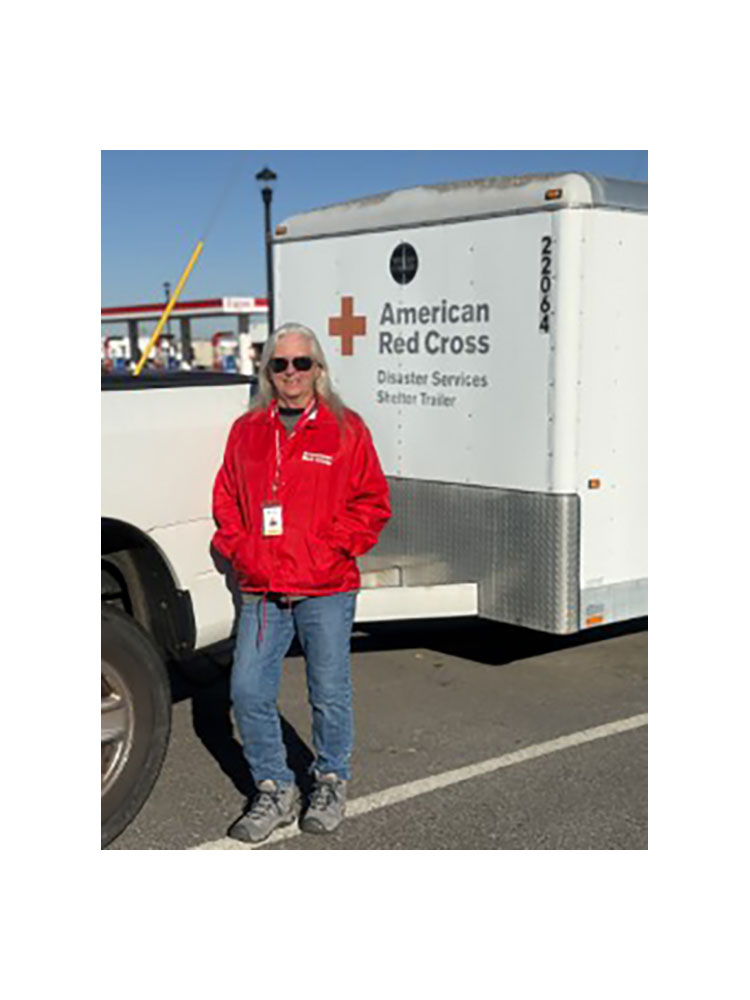 Kim Wilson wearing sunglasses and a Red Cross jacket while standing next to a Red Cross trailer.