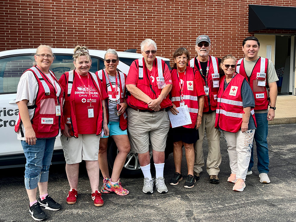 Group photo of eight Red Cross volunteers standing next to a Red Cross vehicle.