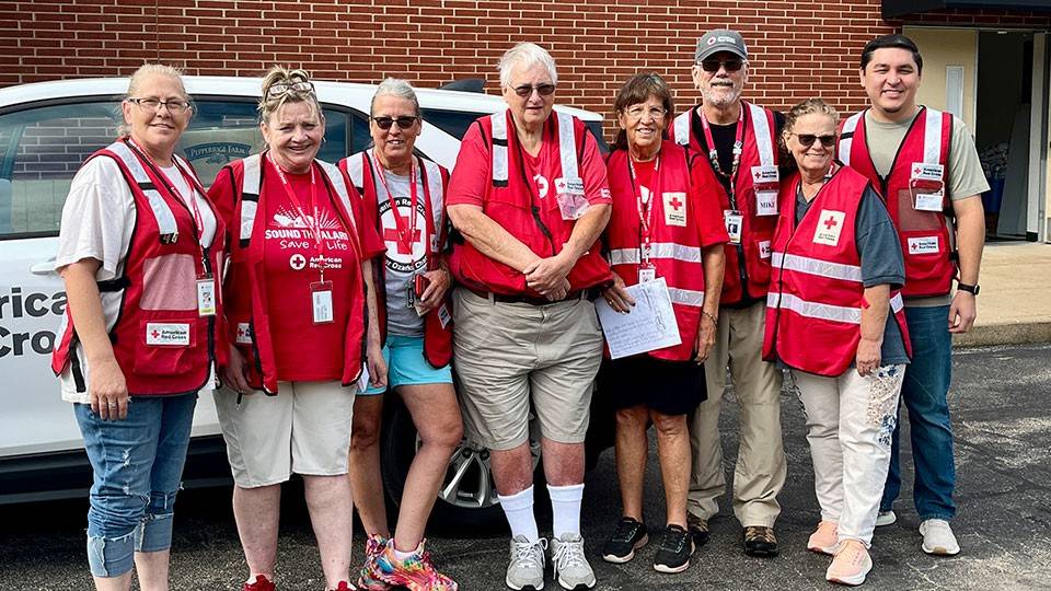 Group photo of eight Red Cross volunteers standing next to a Red Cross vehicle.