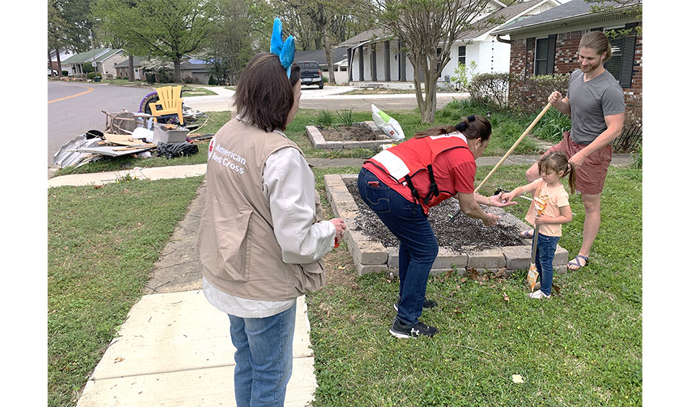 Red Cross volunteer handing candy to little girl who's next to her dad