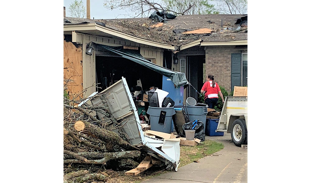 Red Cross volunteer in front of damaged house