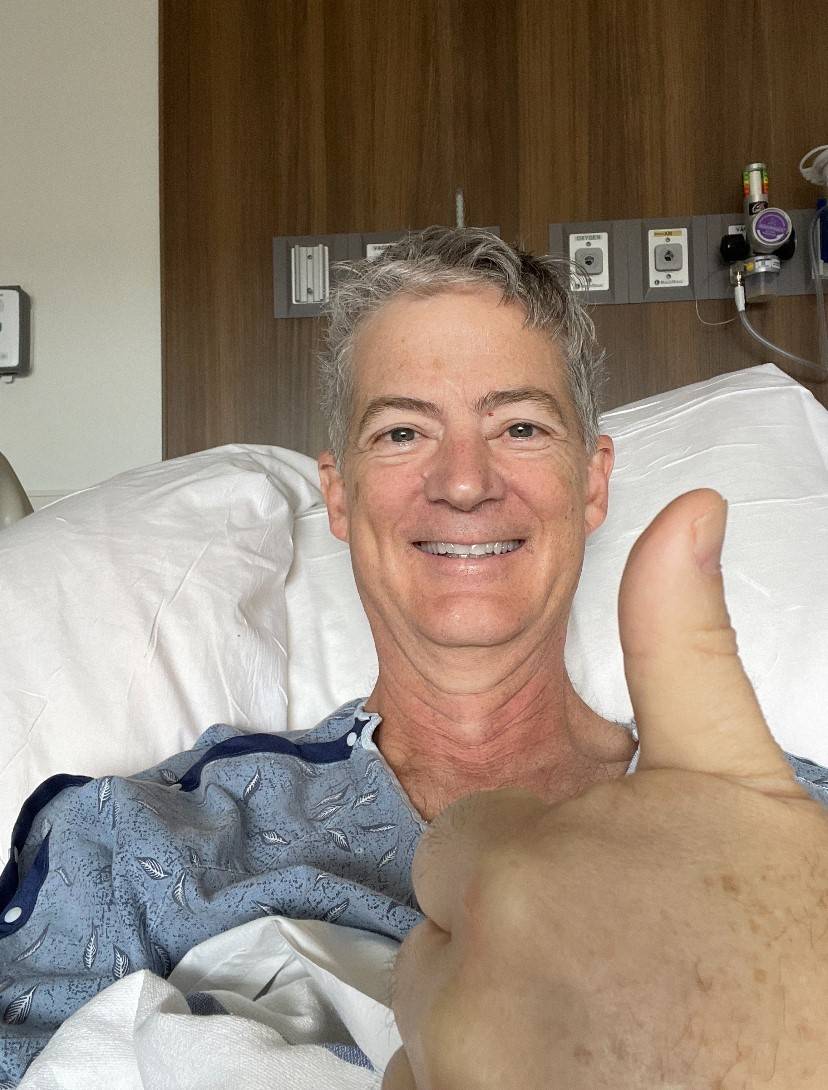 man laying in hospital bed giving a thumbs up