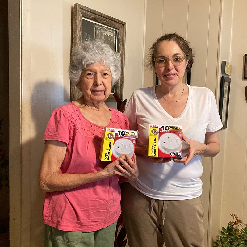 Two woman holding new smoke alarms.