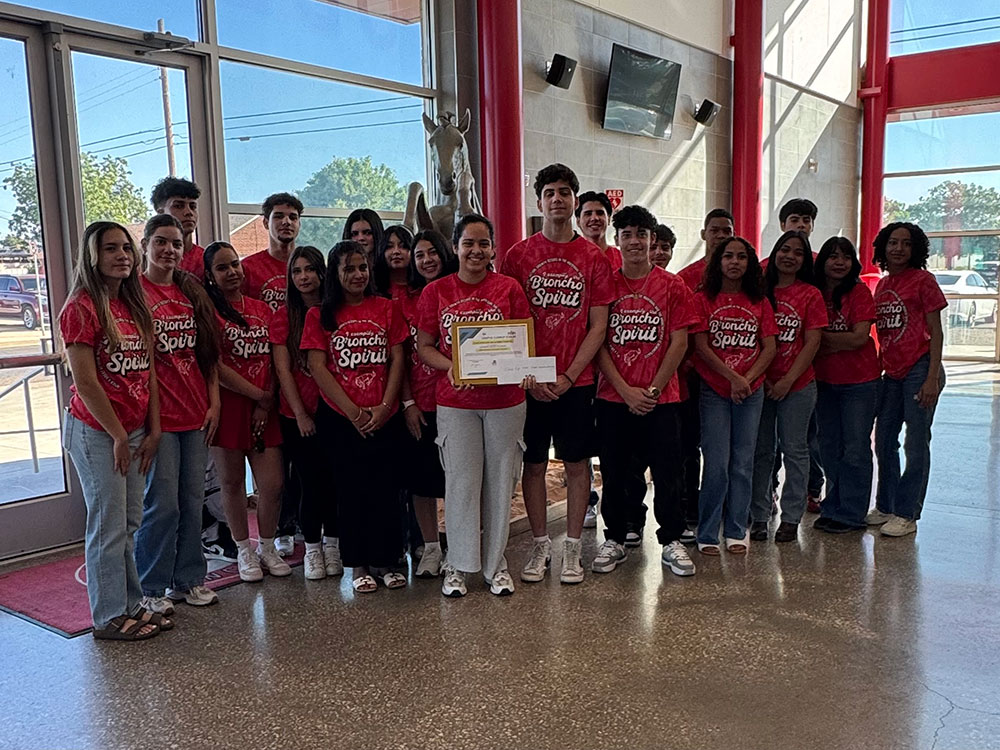 A group of Odessa High School students wearing red broncho spirit shirts stands together inside a building, smiling and posing for the photo.