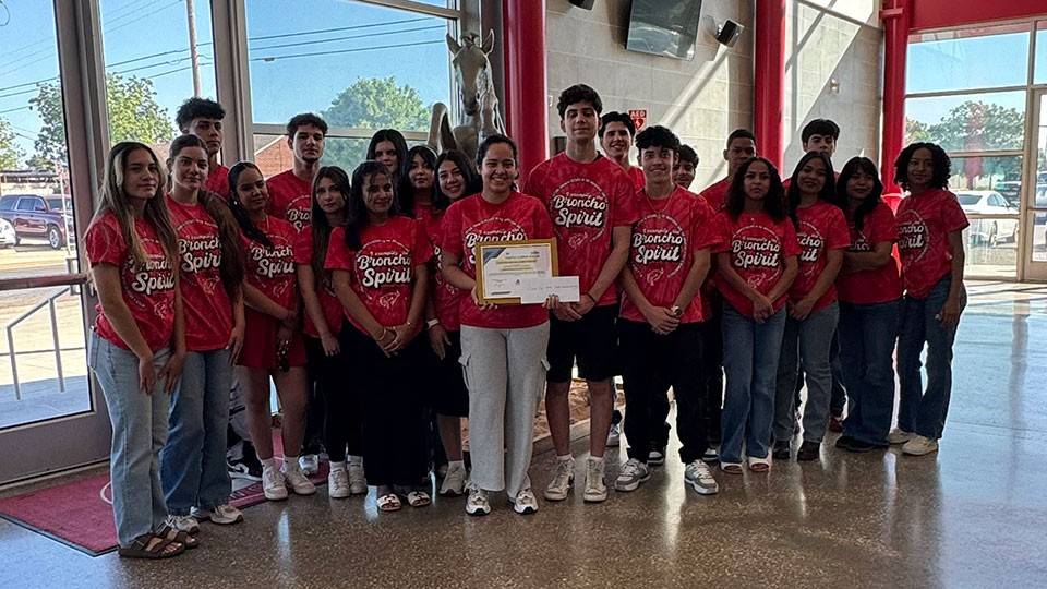 A group of Odessa High School students wearing red broncho spirit shirts stands together inside a building, smiling and posing for the photo.
