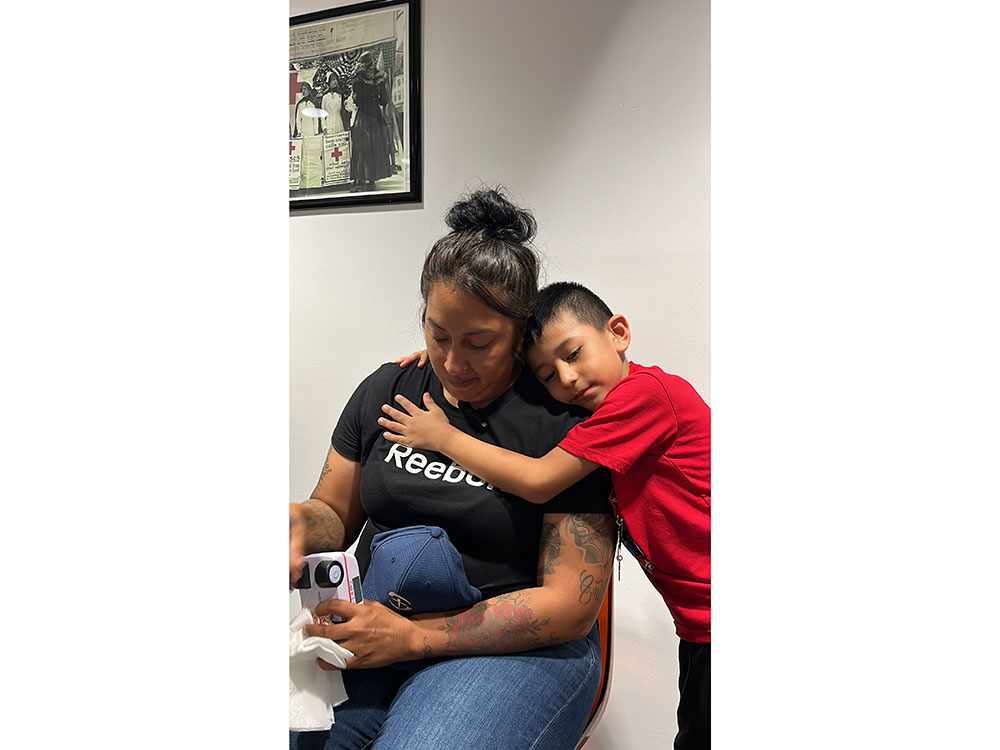 a son hugging his mother who is sitting in a chair holding a Red Cross CPR compression tool.