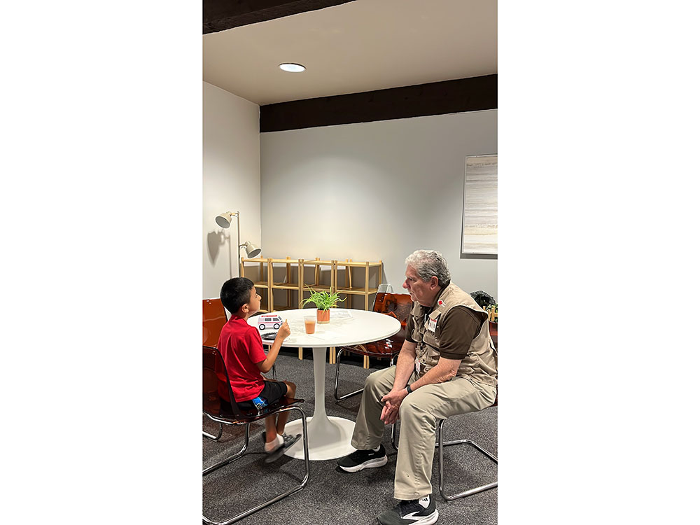 a Red Cross volunteer sitting and talking with a child at a table.